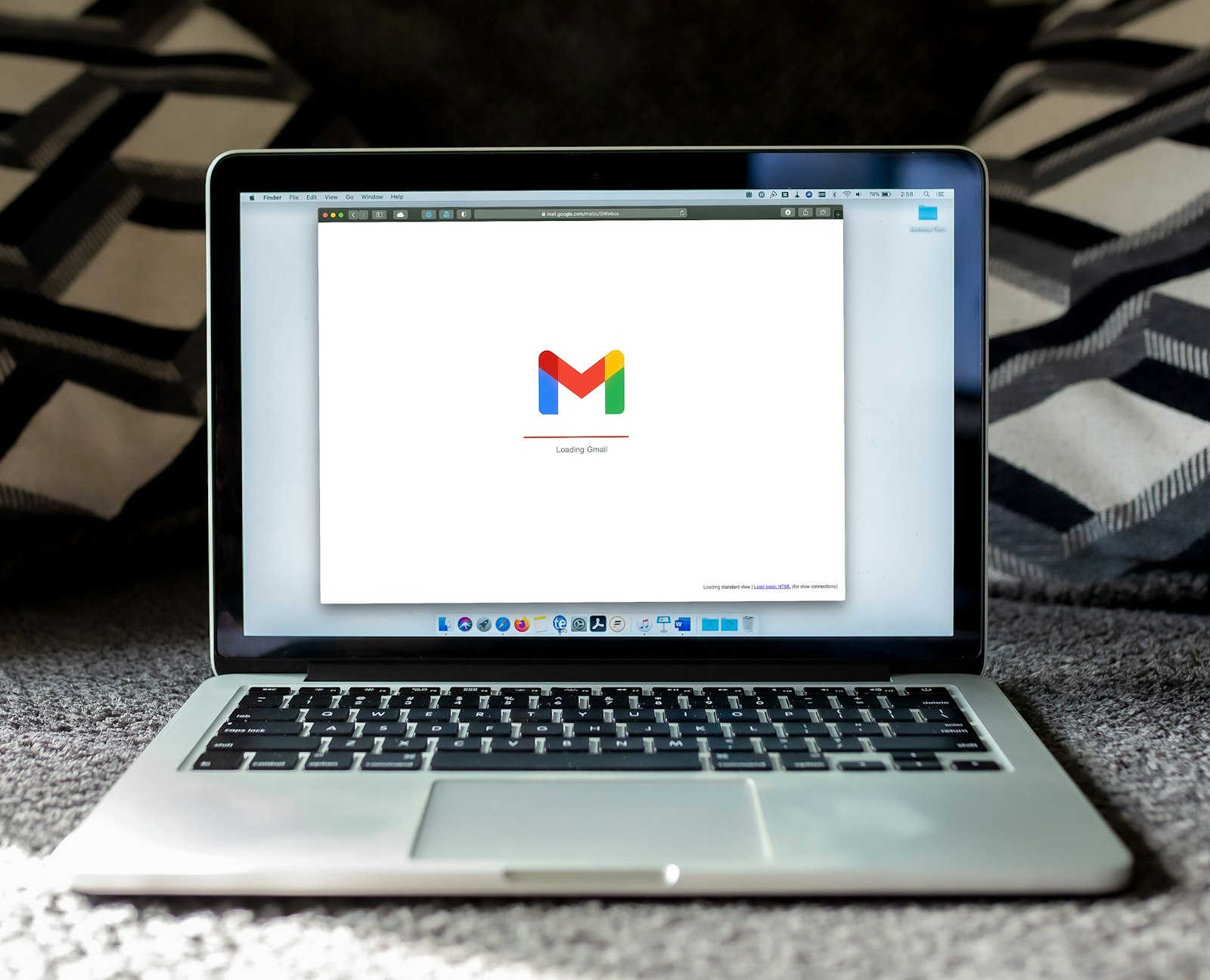 MacBook on a dark rug with the Gmail logo loading on screen