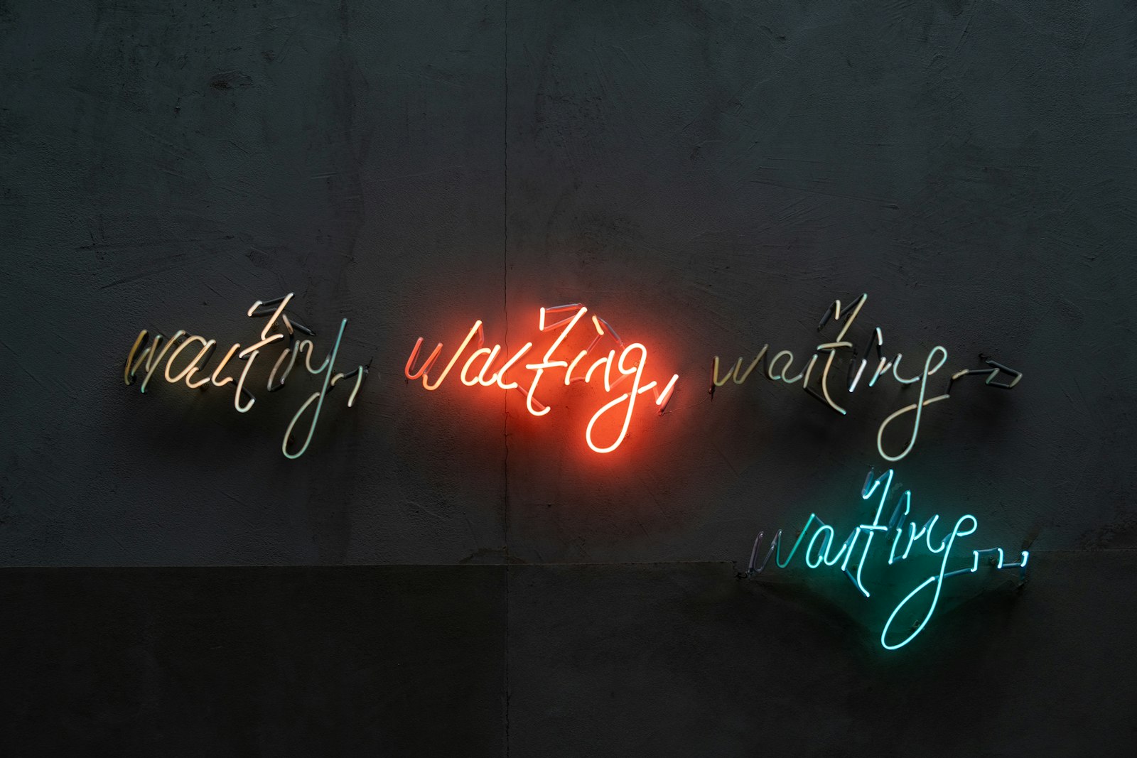 Neon sign repeating the word 'waiting' in different colors against a dark wall
